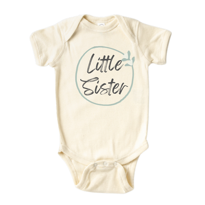 Natural Baby Onesie with a minimalistic printed graphic of a pastel green floral wreath and the text 'Little Sister.' This charming t-shirt celebrates the joyous arrival of a little sister.