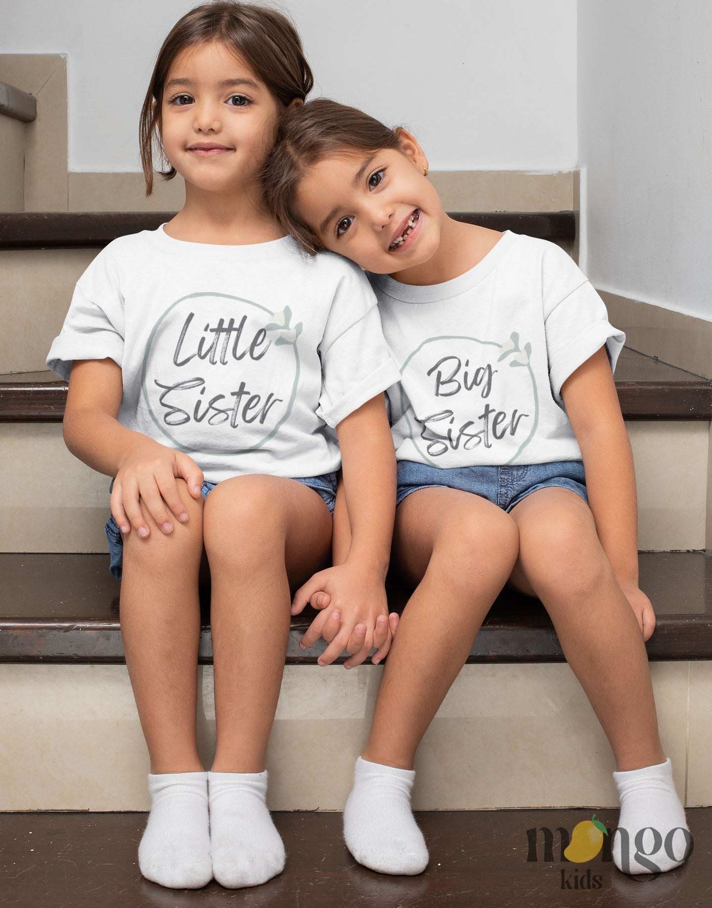 A kid's t-shirt with a minimalistic printed graphic of a pastel green floral wreath and the text 'Little Sister.' This charming t-shirt celebrates the joyous arrival of a little sister.