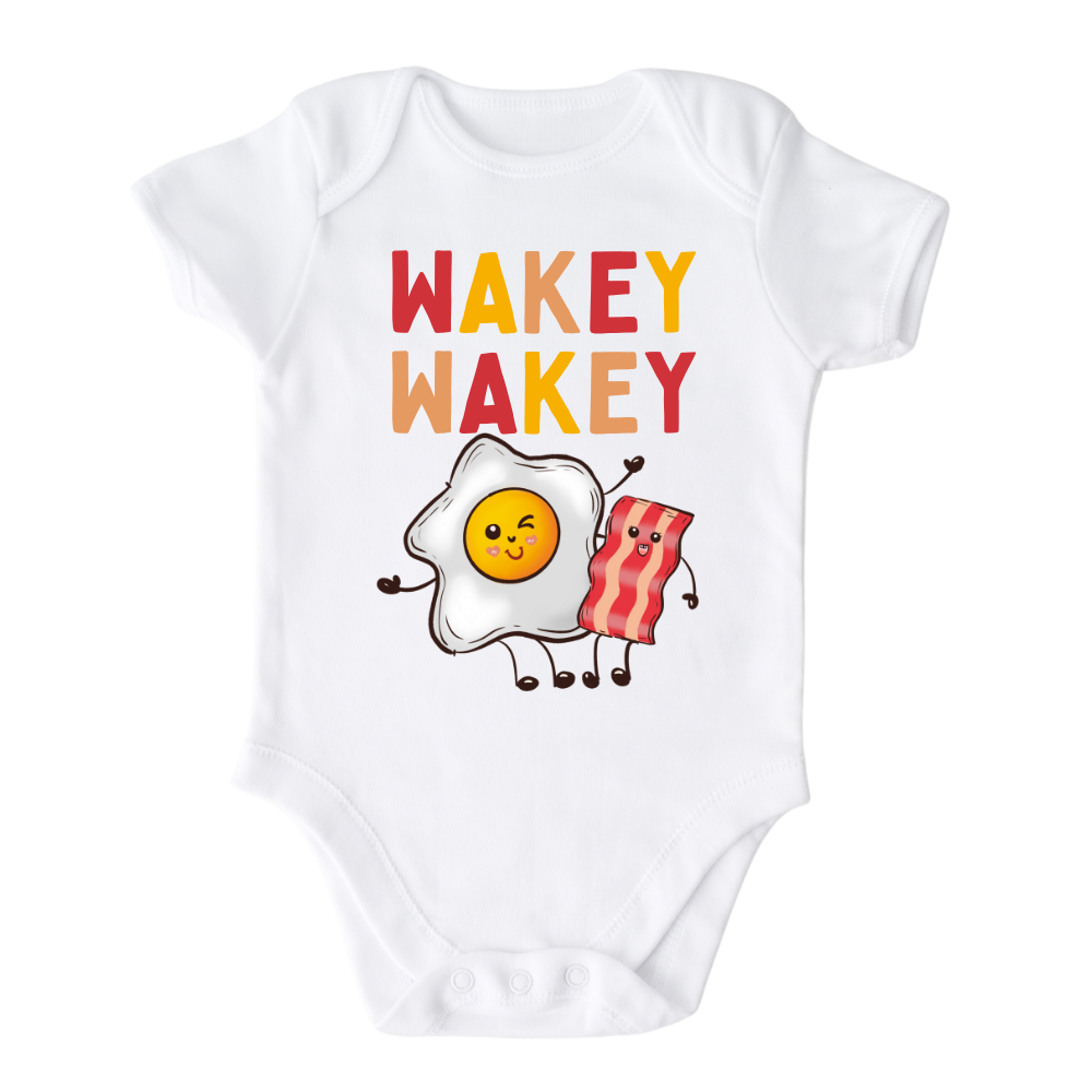 White Baby Onesie with a charming graphic of an egg and bacon, accompanied by the text 'Wakey Wakey.' Ideal for children who love breakfast and waking up with a smile. 