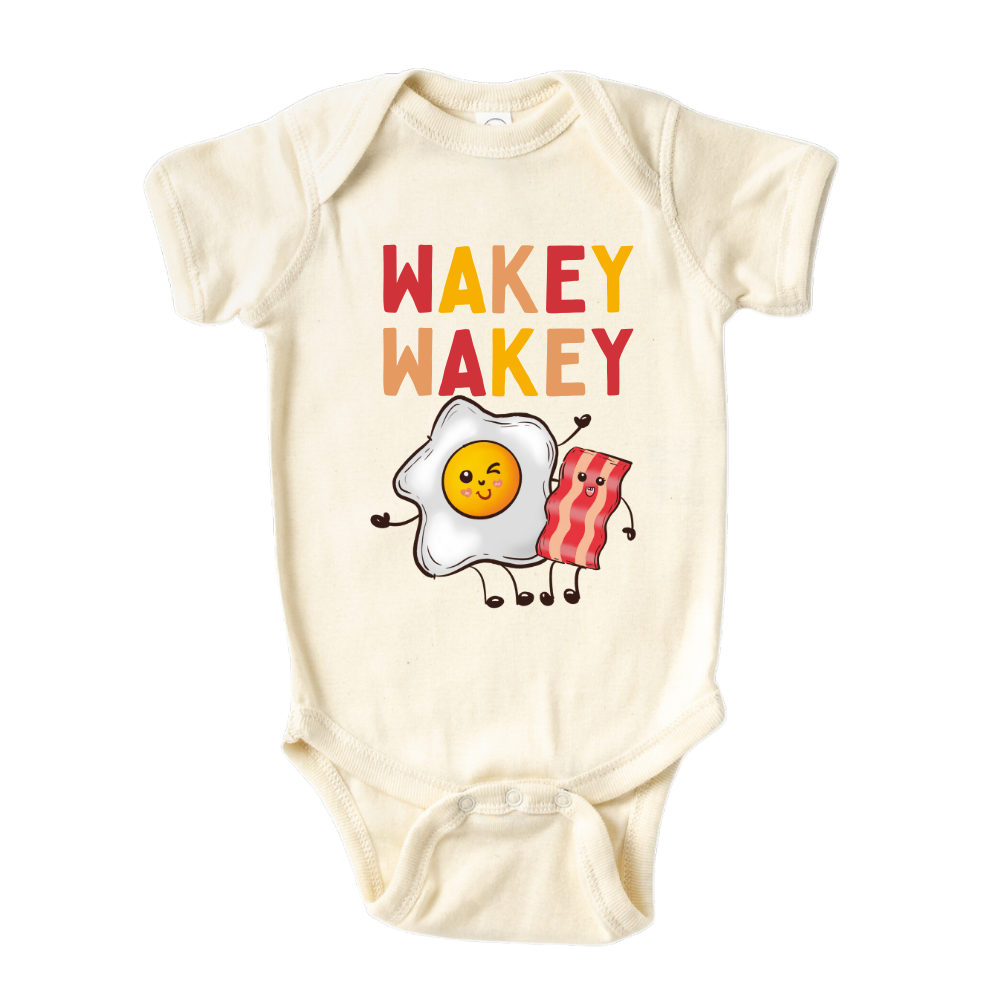 Natural Baby Bodysuit with a charming graphic of an egg and bacon, accompanied by the text 'Wakey Wakey.' Ideal for children who love breakfast and waking up with a smile. 