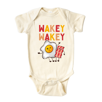 Natural Baby Bodysuit with a charming graphic of an egg and bacon, accompanied by the text 'Wakey Wakey.' Ideal for children who love breakfast and waking up with a smile. 