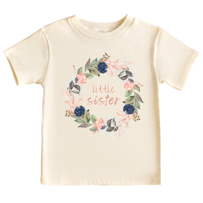 Natural kid's t-shirt with a cute printed graphic of a floral wreath and the text 'Little Sister.' This adorable t-shirt celebrates the arrival of a precious little sister.