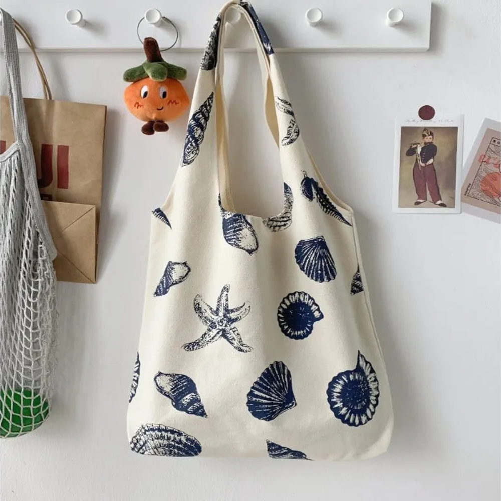 front view of beige color canvas tote bag with dark blue prints of seashells and ocean star icons