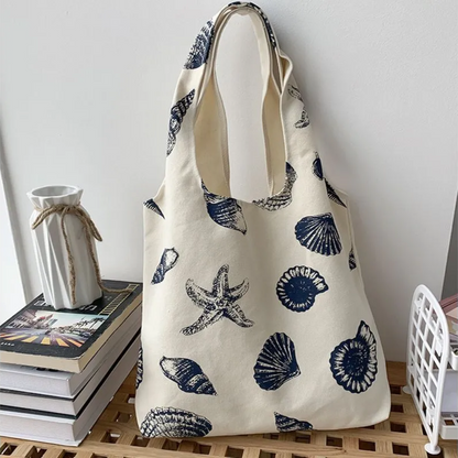 front view of beige color canvas tote bag with dark blue prints of seashells and ocean star icons